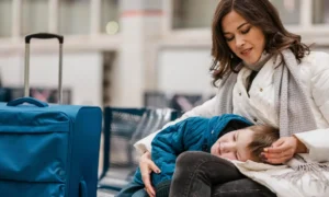 Mãe e filho aguardando no aeroporto com malas de viagem, representando a tranquilidade de viajar protegido com o seguro viagem obrigatório para a Itália.