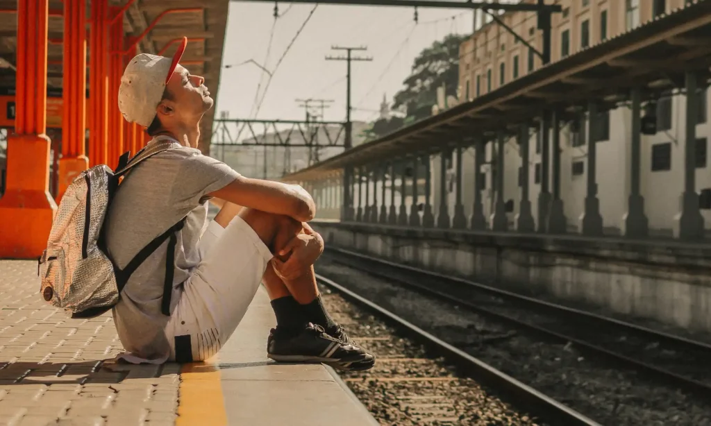 Viajante com mochila sentado na plataforma de uma estação ferroviária aguardando o embarque, ilustrando como viajar de trem na Itália com tranquilidade.